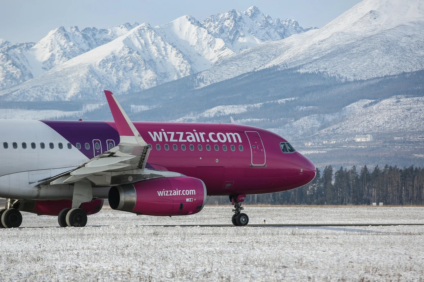 Wizz Air poleci z Gdańska w Tatry Różowy samolot pasażerski linii Wizzair na pasie startowym, w tle ośnieżone górskie szczyty i zimowy krajobraz.