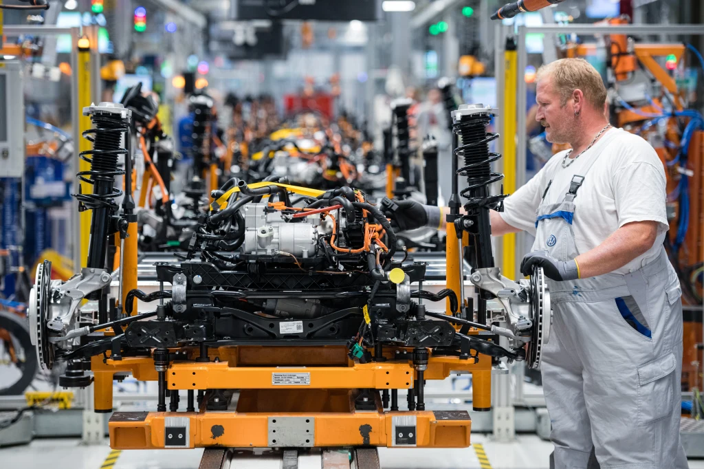 Do produkcji samochodów elektrycznych potrzebne są m.in. wolfram, złoto i cyna. Wydobycie i handel tymi pierwiastkami nie zawsze są legalne Montaż silnika i części zawieszenia w nowoczesnej fabryce motoryzacyjnej, pracownik ubrany w biały kombinezon nadzoruje precyzyjne procesy produkcyjne na linii montażowej.