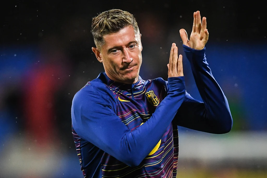 Robert Lewandowski Mężczyzna w sportowej bluzie klaszcze dłońmi, patrząc w stronę aparatu, na tle rozmytego stadionu.