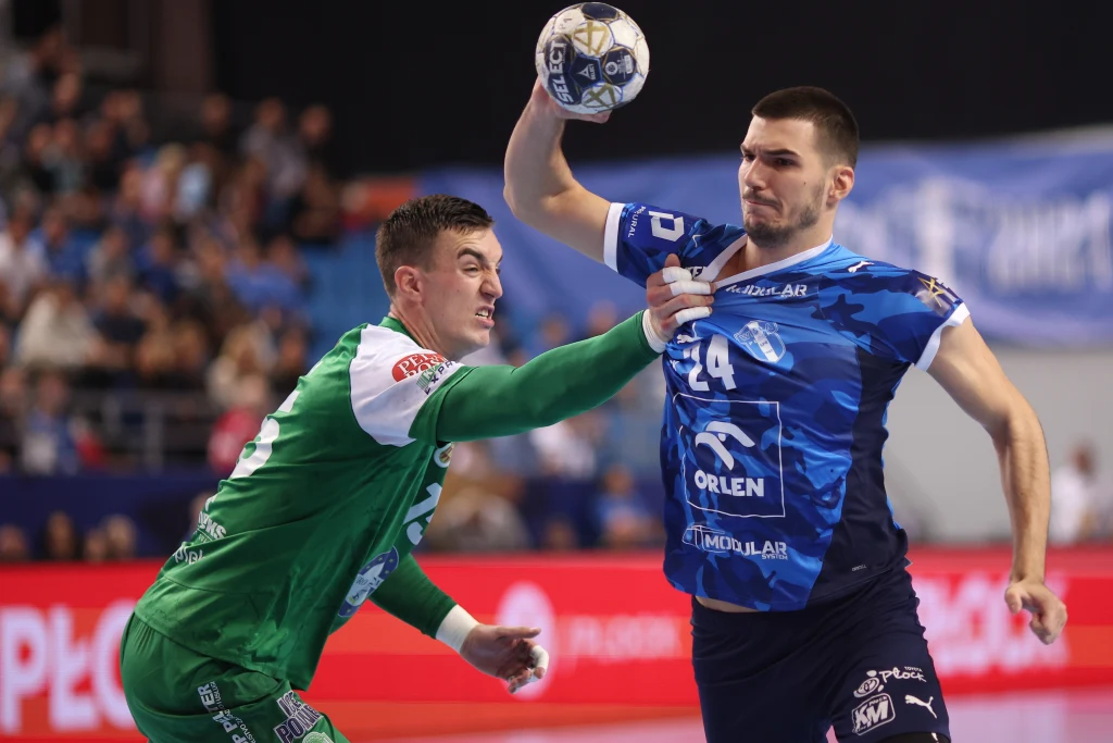 Gergo Fazekas w meczu z Eurofarmem Dwóch zawodników piłki ręcznej w trakcie pojedynku na boisku, zawodnik w niebieskiej koszulce z piłką wznosi rękę do rzutu, zawodnik w zielonym stroju próbuje go zablokować.