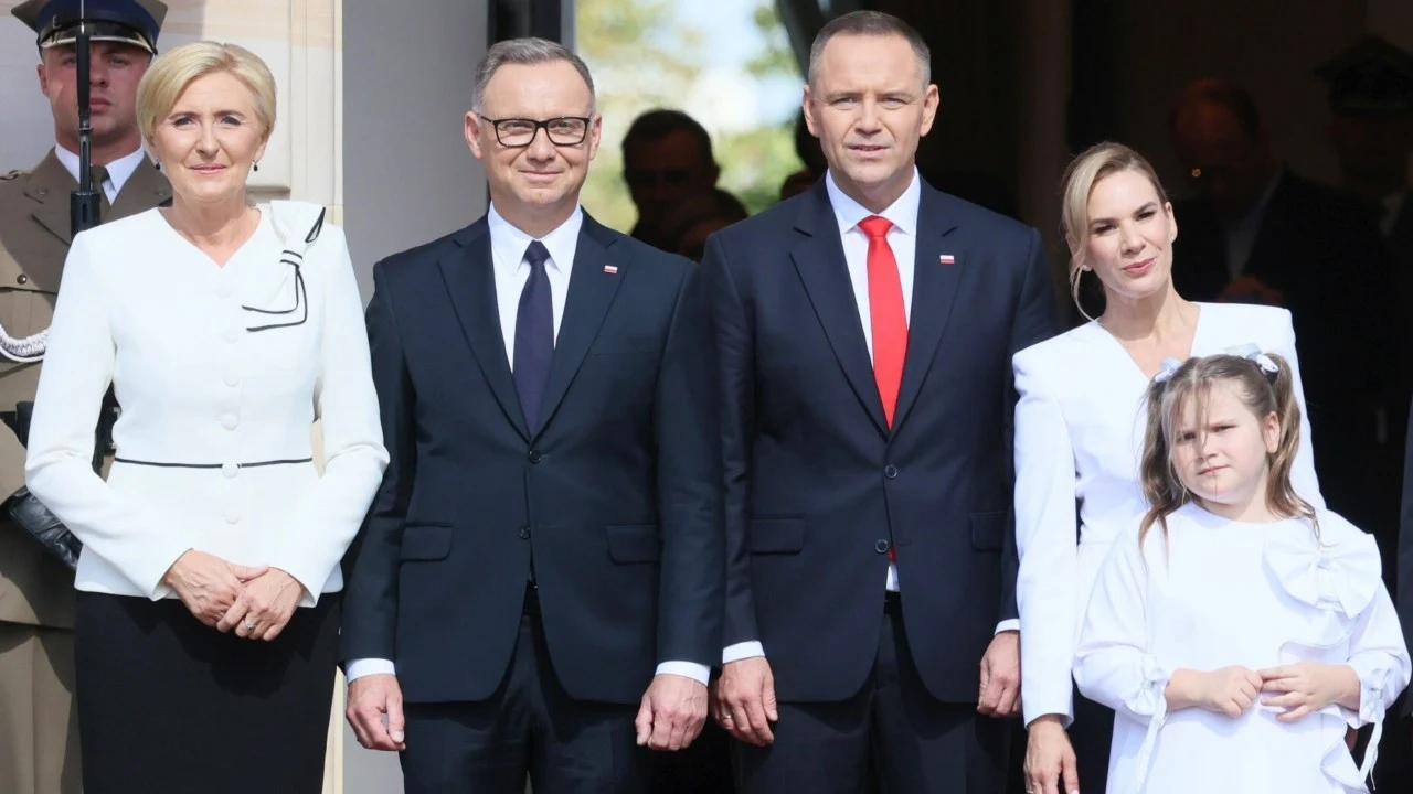 W PiS-ie nie mają złudzeń: partia nie będzie w stanie kontrolować Karola Nawrockiego tak, jak kontrolowała Andrzeja Dudę Grupa pięciu osób ubranych elegancko stoi razem przed wejściem do budynku, dwie kobiety i dziewczynka w białych strojach oraz dwaj mężczyźni w ciemnych garniturach z przypiętymi polskimi flagami, w tle widoczny żołnierz.