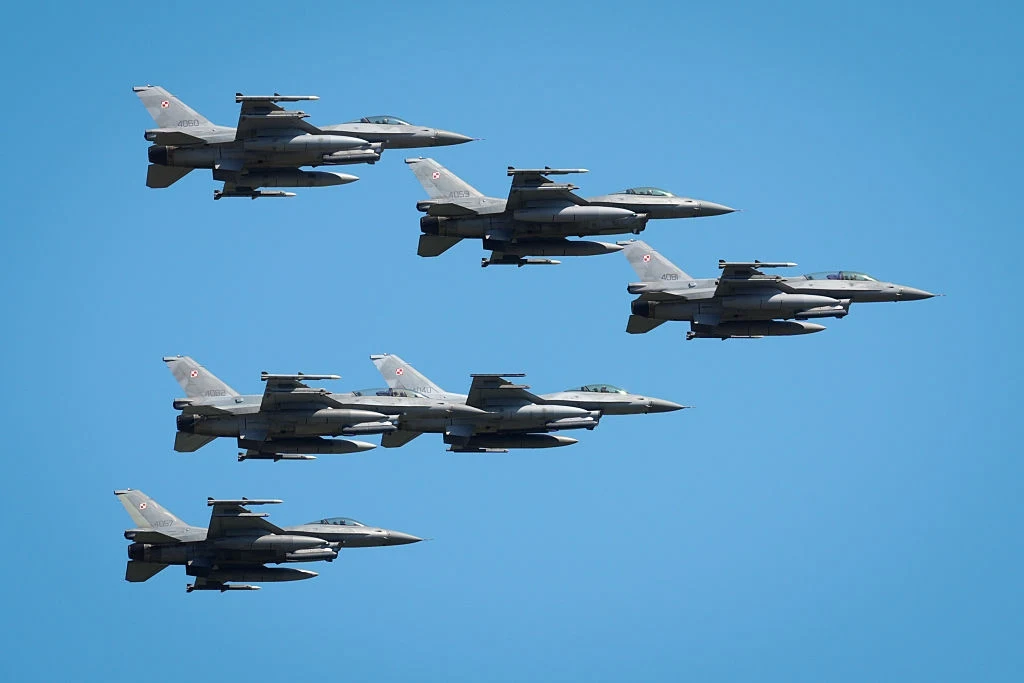 Piloci NATO są w ciągłej gotowości Sześć myśliwców wojskowych F-16 leci w zwartej formacji na tle bezchmurnego, niebieskiego nieba.