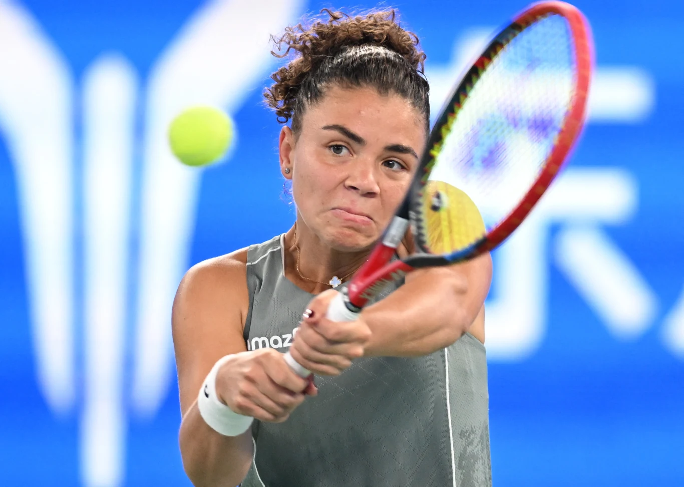 Jasmine Paolini, Wuhan 2025 Tenisistka podczas dynamicznego uderzenia piłki rakietą, skoncentrowana na grze, w tle rozmazany niebieski kort.