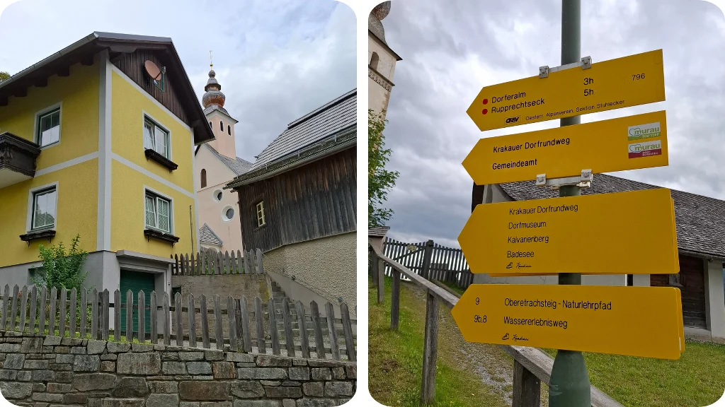 Żółty dom z ogrodzeniem z drewnianych sztachet, w tle budynek kościelny z wieżą i kopułą, po prawej żółte tablice informacyjne z nazwami szlaków turystycznych oraz kierunkami.