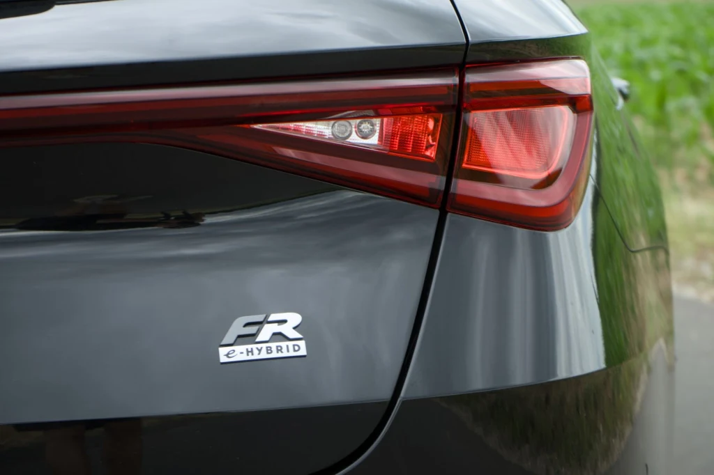 Seat Leon z hybrydą plug-in dostępny jest tylko w wyższym wariancie wyposażenia - FR. Tylny reflektor samochodu, logo FR e-HYBRID, połyskujący lakier, fragment tylnej klapy i drogi w tle.