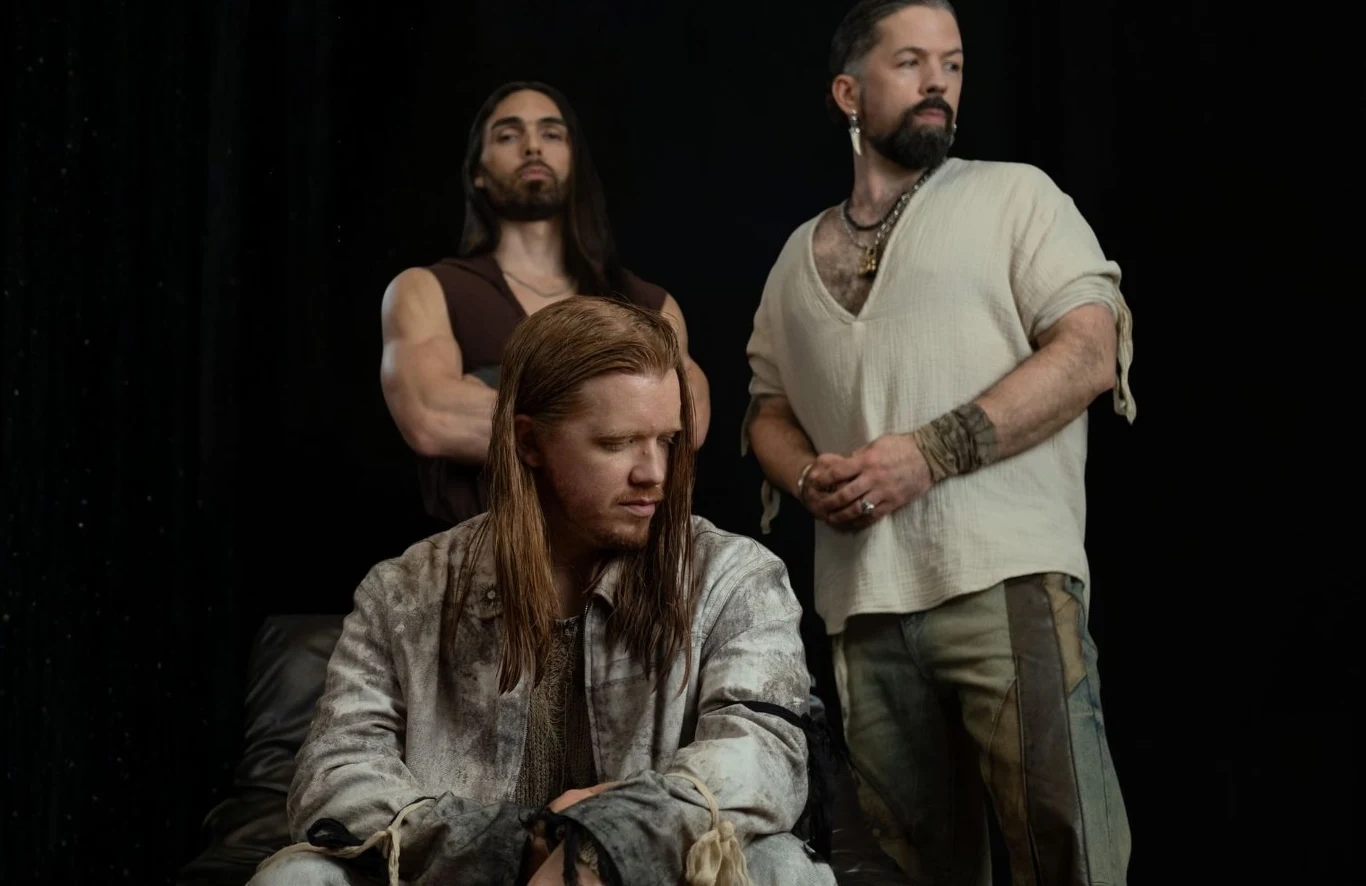 Equilibrium powracają z nowym albumem Trzech mężczyzn w stylizowanych, nieformalnych strojach, ustawionych w ciemnej scenerii; jeden siedzi ze spuszczoną głową i długimi włosami, dwóch stoi za nim, podkreślając wrażenie skupienia i siły.