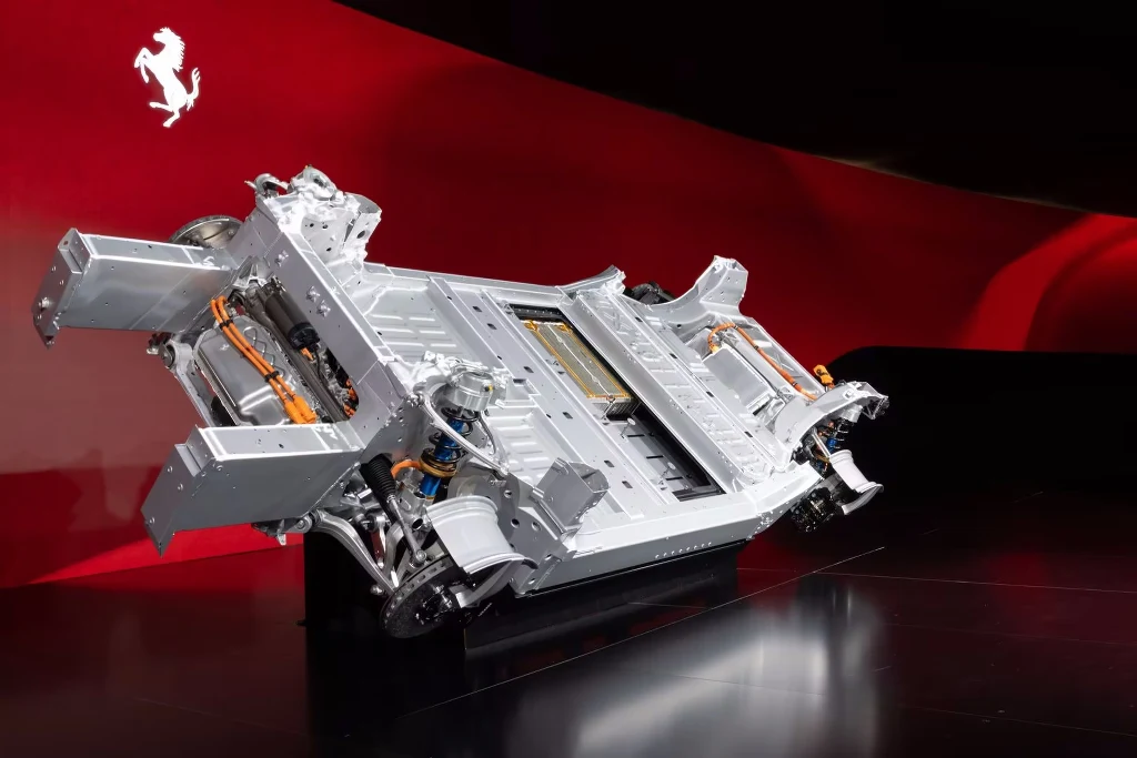 Platforma, na której zbudowane zostanie Ferrari Elettrica Podwozie elektrycznego samochodu Ferrari wyeksponowane na tle czerwonej ściany z charakterystycznym logo marki, widoczne elementy konstrukcyjne, akumulatory i przewody elektryczne.