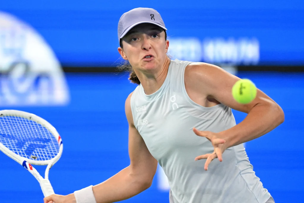 Iga Świątek rywalizowała z Belindą Bencić o awans do ćwierćfinału WTA 1000 w Wuhan Tenisistka w sportowej czapce i jasnym stroju wykonuje zamach rakietą, koncentrując wzrok na nadlatującej piłce podczas intensywnego meczu na tle niebieskiego kortu.