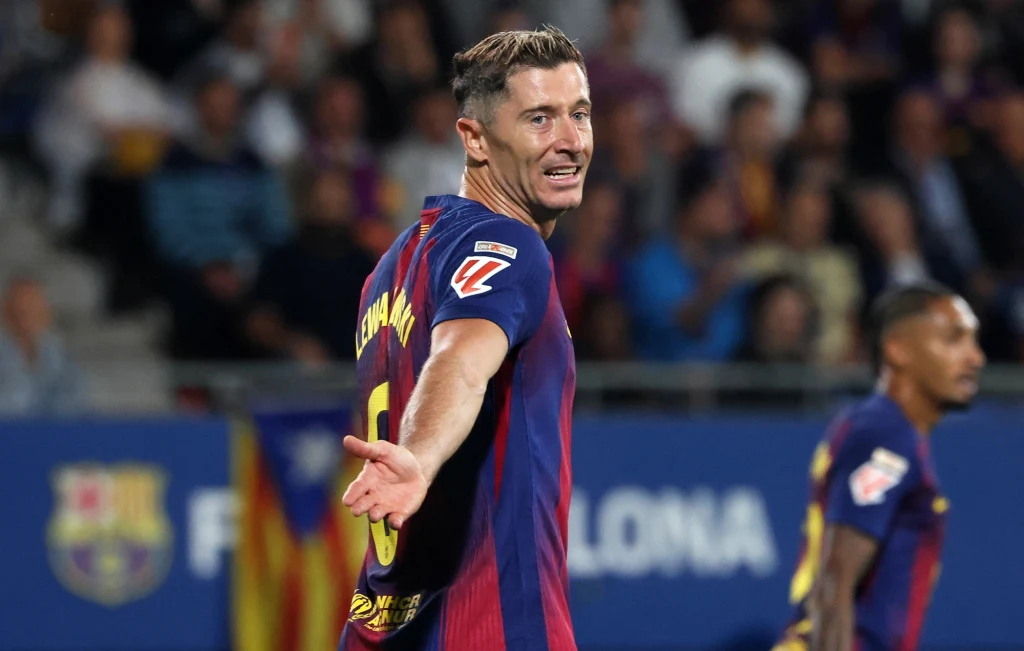 Robert Lewandowski Piłkarz w granatowo-bordowej koszulce z napisem na plecach gestykuluje podczas meczu, w tle widoczny jest rozmazany stadion oraz inni zawodnicy.