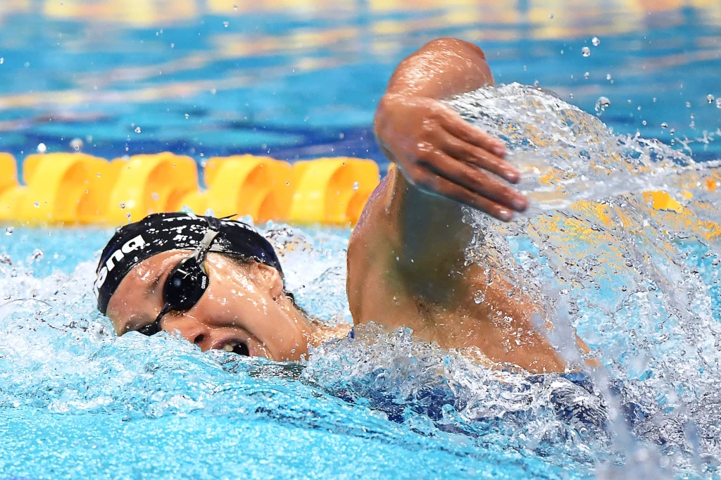 Chiara Tarantino Zawodnik w okularach pływackich i czepku płynie stylem dowolnym w basenie, rozpryskując wodę podczas dynamicznego ruchu ramienia