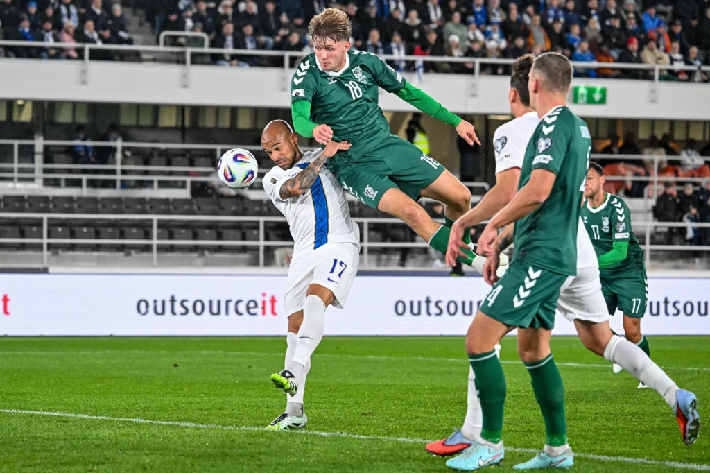 W Helsinkach skazywana na zagładę reprezentacja Litwy nie ograniczała się wyłącznie do destrukcji Piłkarz w zielonym stroju unosi się w powietrzu, uderzając piłkę głową podczas walki o piłkę z przeciwnikiem w białym stroju, na tle stadionu wypełnionego kibicami.