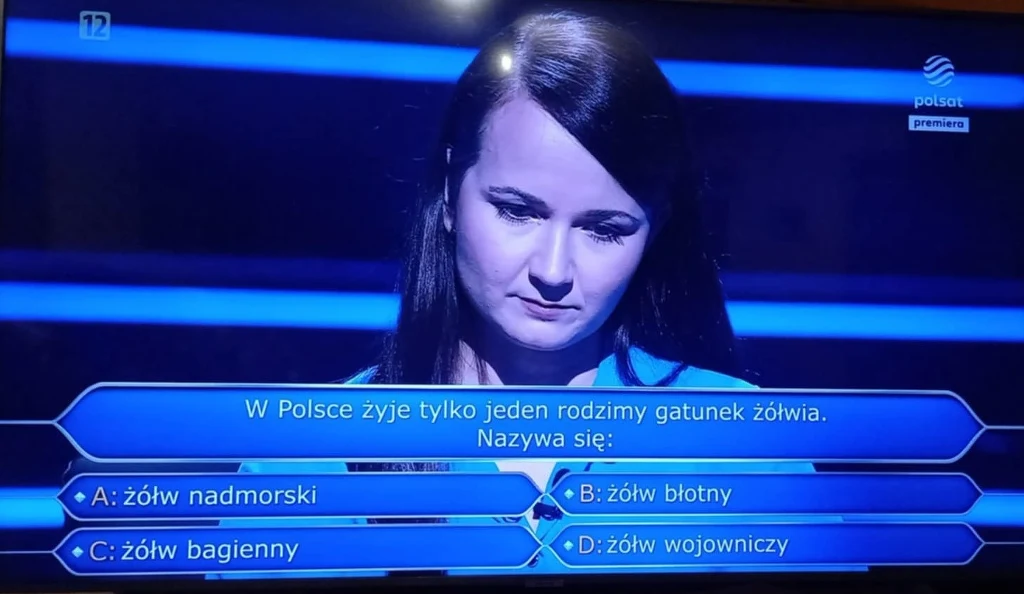 Kobieta bierze udział w teleturnieju wiedzy, na ekranie widoczne pytanie dotyczące rodzimego gatunku żółwia w Polsce oraz cztery możliwe odpowiedzi.