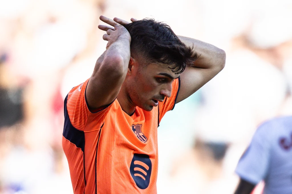 Pedri Młody mężczyzna w pomarańczowej koszulce sportowej trzyma ręce za głową, wyrażając skupienie i emocje na boisku w trakcie meczu.