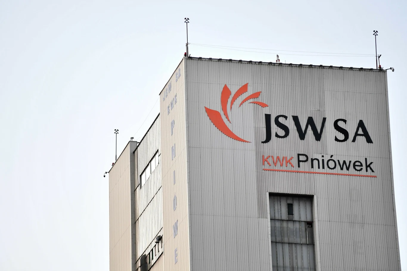 Związkowcy z JSW chcą, aby rozmowy o restrukturyzacji poprzedziła pełna informacja o stanie spółki. Uważają też, że większe pole do cięć jest w administracji Fragment elewacji budynku przemysłowego z wyraźnie widocznymi napisami JSW SA oraz KWK Pniówek, logo firmy górniczej i elementami infrastruktury na dachu.