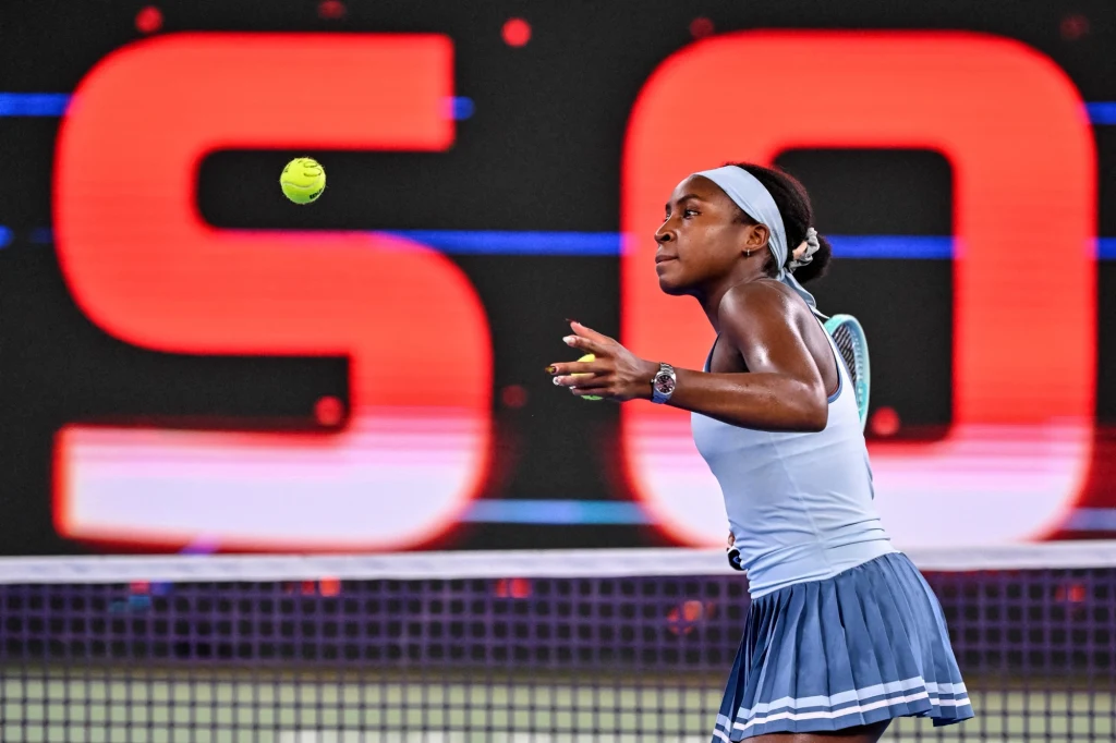 Coco Gauff, Wuhan 2025 Tenisistka w trakcie dynamicznego meczu koncentruje się na piłce lecącej nad siatką, z tłem w postaci rozświetlonego napisu.