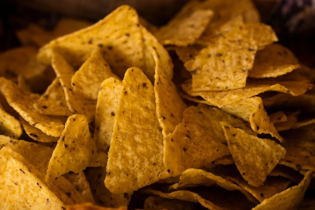 Stos żółtych, chrupiących nachos z wyraźnie widoczną fakturą, rozmieszczonych warstwowo jedno na drugim.