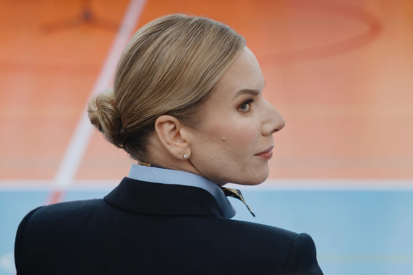 Marta Nawrocka zadała szyku stylizacją w Estonii. Jej marynarka zrobiła furorę w sieci Kobieta z upiętymi włosami w schludnym mundurze, skierowana w bok, z tłem w intensywnych kolorach pomarańczowym i niebieskim typowym dla hali sportowej.