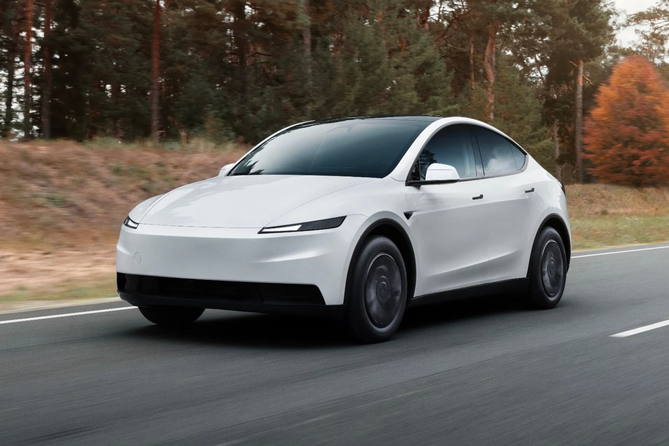Biały nowoczesny samochód elektryczny jedzie po asfaltowej drodze otoczonej lasem iglastym, tło rozmyte od szybkości pojazdu, wyraźnie widoczne aerodynamiczne kształty nadwozia.