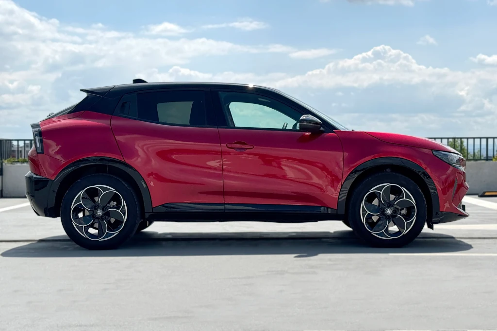 Czerwony, nowoczesny samochód typu crossover zaparkowany na otwartym parkingu z widokiem na niebo i chmury w tle.