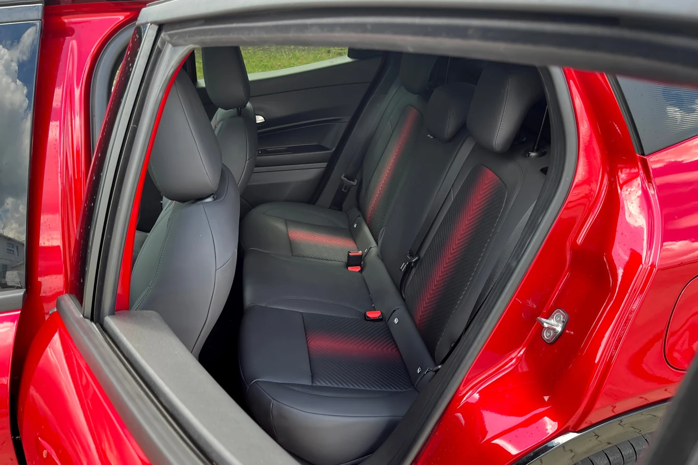 Za wysokim kierowcą w Alfie Junior może być ciasno Czerwony samochód z szeroko otwartymi tylnymi drzwiami, widok na czarne siedzenia tylnej kanapy z wyraźnymi pasami bezpieczeństwa i nowoczesnym wykończeniem
