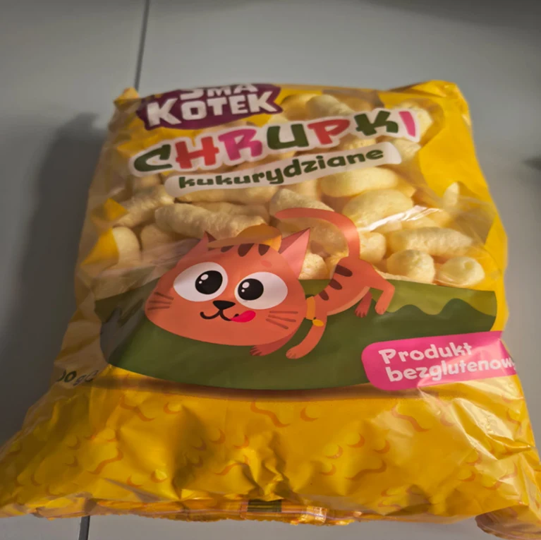 GIS ostrzega przed chrupkami bezglutenowymi - wykryto w nich gluten Opakowanie żółtych chrupków kukurydzianych z rysunkiem uśmiechniętego kota, wyraźnym napisem Chrupki kukurydziane, informacją o produkcie bezglutenowym na jasno różowym tle oraz nazwą marki Smak Kotek.