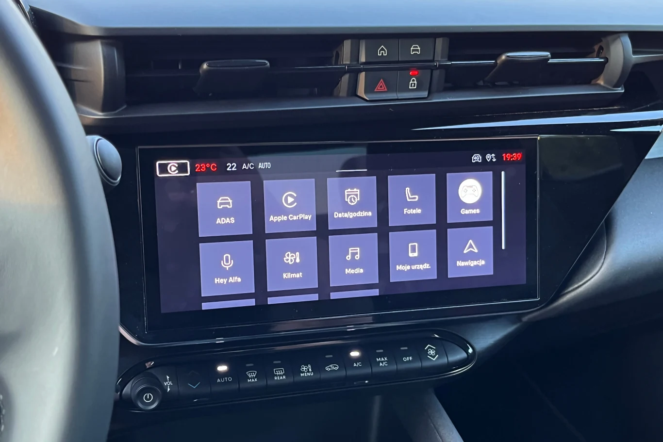 Taki sam ekran systemu infotainment znajdziemy w szeregu innych modeli Stellantisa. Podobnie jak znajdujący się wyżej panel czterech fizycznych przycisków Nowoczesny ekran dotykowy systemu multimedialnego w samochodzie, wyświetlający menu z ikonami różnych funkcji, takich jak Apple CarPlay, radio, media, nawigacja oraz ustawienia. Poniżej ekranu fizyczny panel przycisków klimatyzacji.
