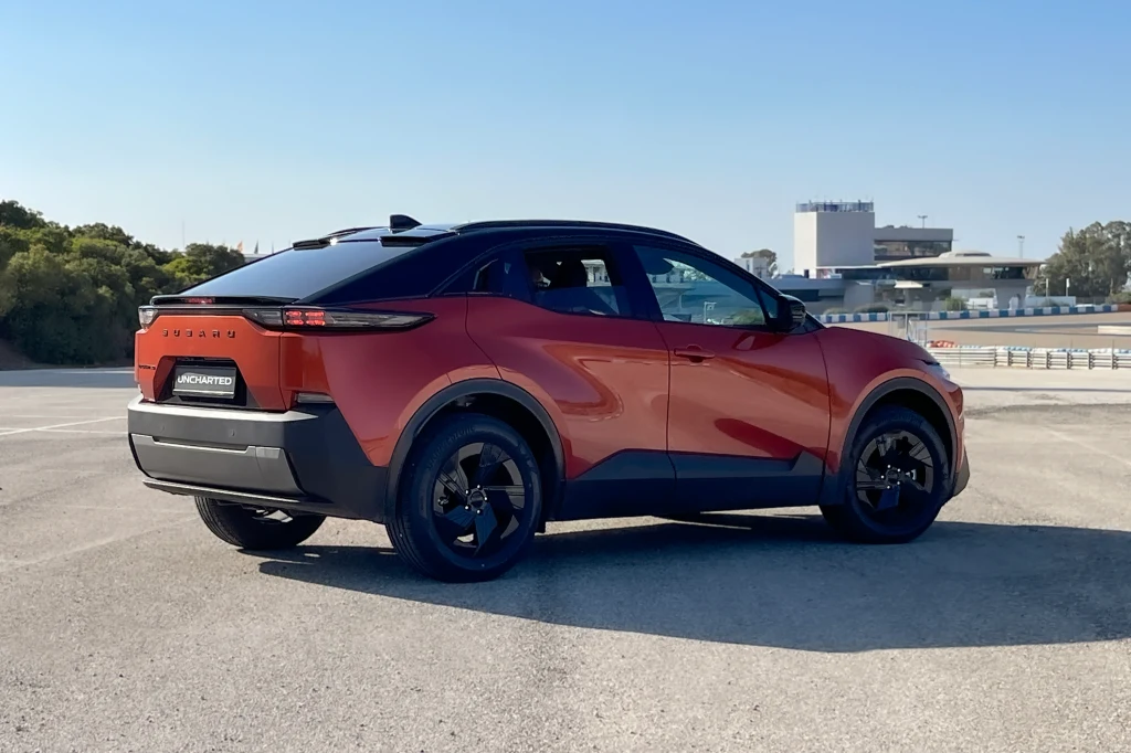 Nowoczesny, czerwony SUV o sportowej sylwetce stoi na pustym parkingu z elementami industrialnymi i zielenią w tle.