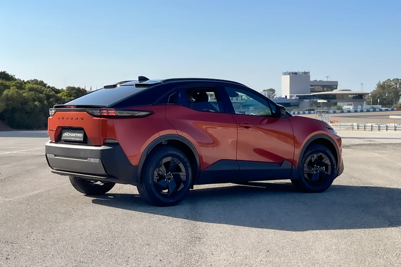 Nowoczesny, czerwony SUV o sportowej sylwetce stoi na pustym parkingu z elementami industrialnymi i zielenią w tle.