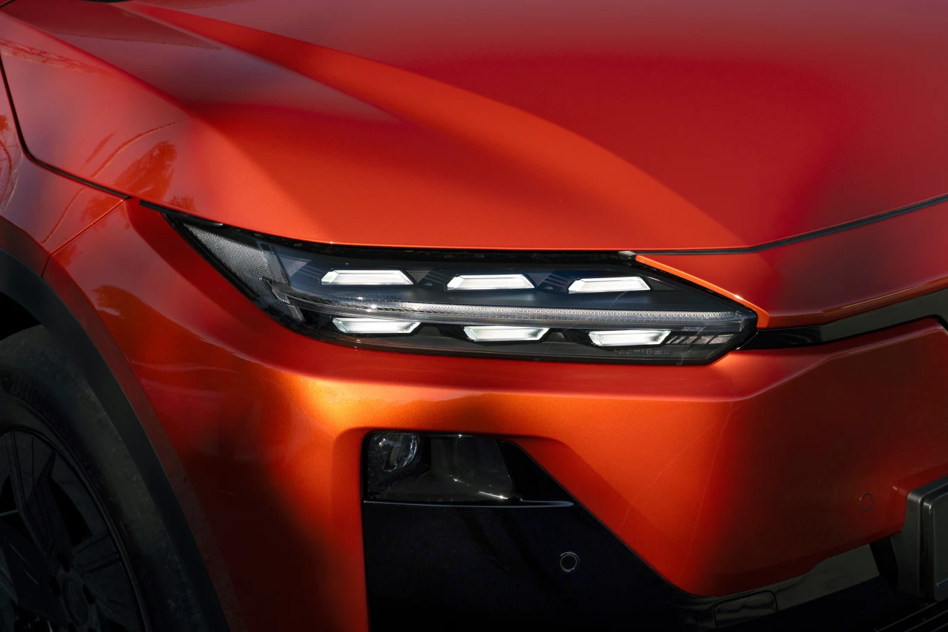 Przedni reflektor nowoczesnego samochodu w czerwonym lakierze, widoczny fragment maski oraz nadkola, detale lampy LED podkreślają dynamiczny charakter pojazdu.