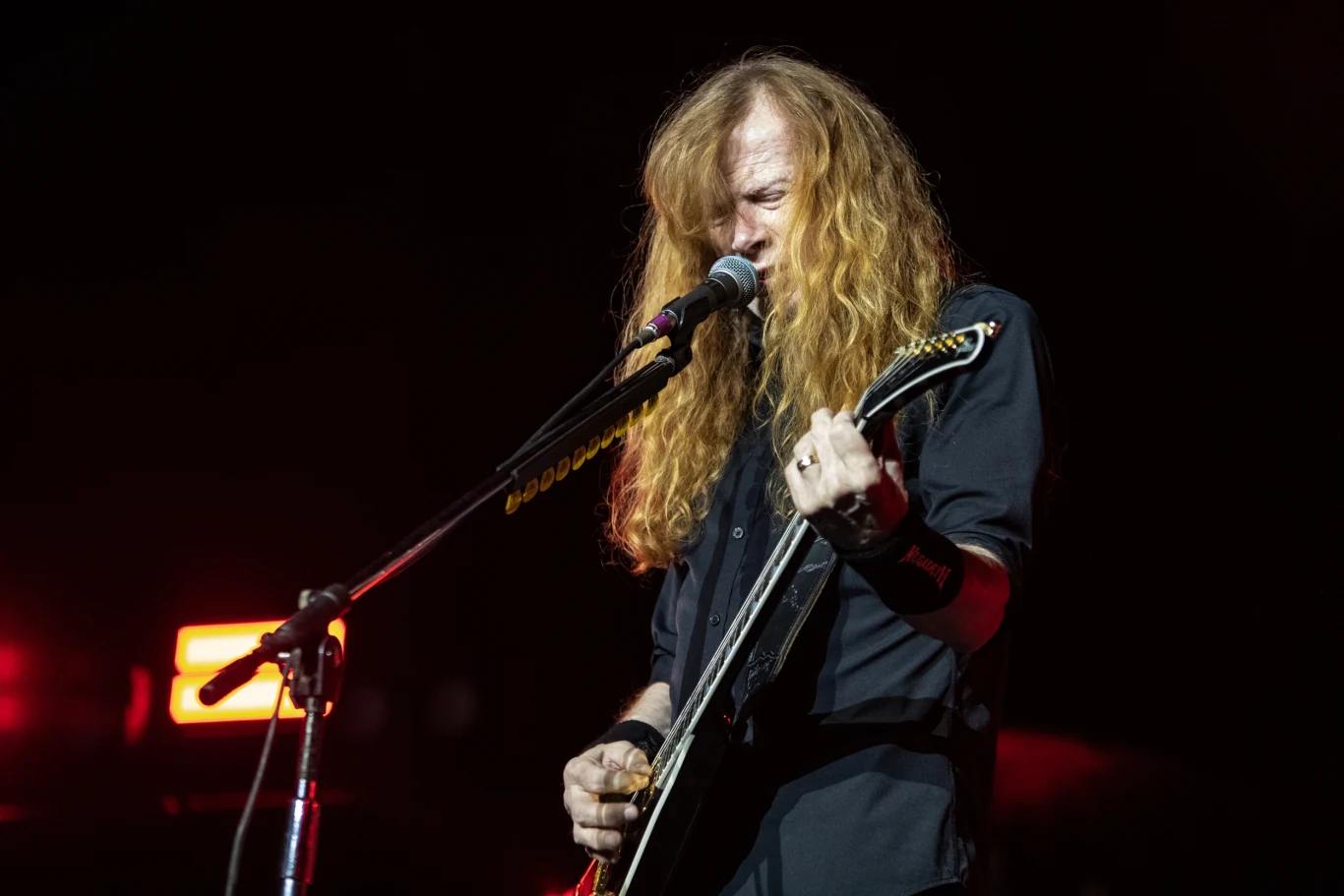 Dave Mustaine (Megadeth) sięgnął po klasyk z dorobku grupy Metallica Mężczyzna z długimi rudymi włosami gra na gitarze elektrycznej i śpiewa do mikrofonu podczas koncertu scenicznego oświetlonego kolorowymi światłami.