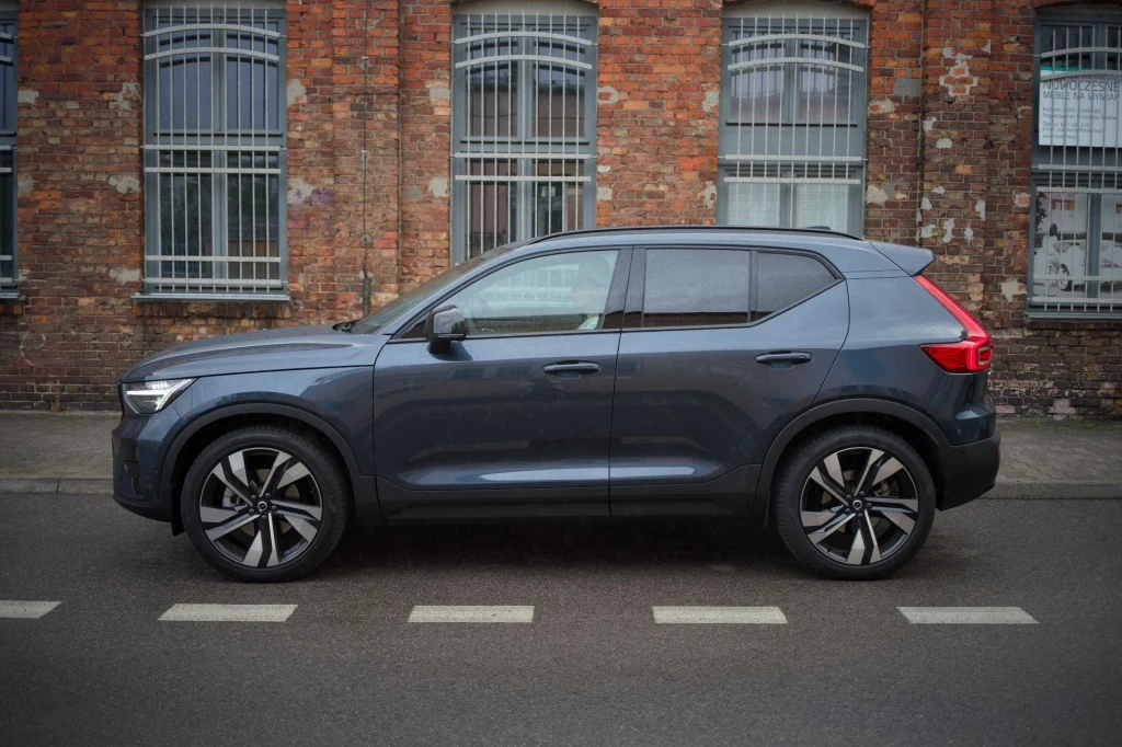 W 2024 roku Volvo XC40 było drugim najchętniej kupowanym modelem tego producenta w Polsce. Nowoczesny, granatowy SUV Volvo XC40 zaparkowany na ulicy przed budynkiem z ceglaną elewacją i dużymi oknami zabezpieczonymi kratami.