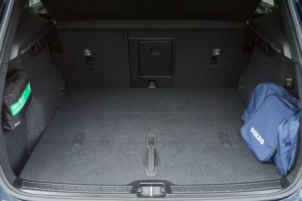 Bagażnik Volvo XC40 przy rozłożonym drugim rzędzie siedzeń może pomieścić do 443 litrów. Przestronny bagażnik samochodu z miękką wykładziną, po lewej stronie zielona apteczka, po prawej torba z logo Volvo.