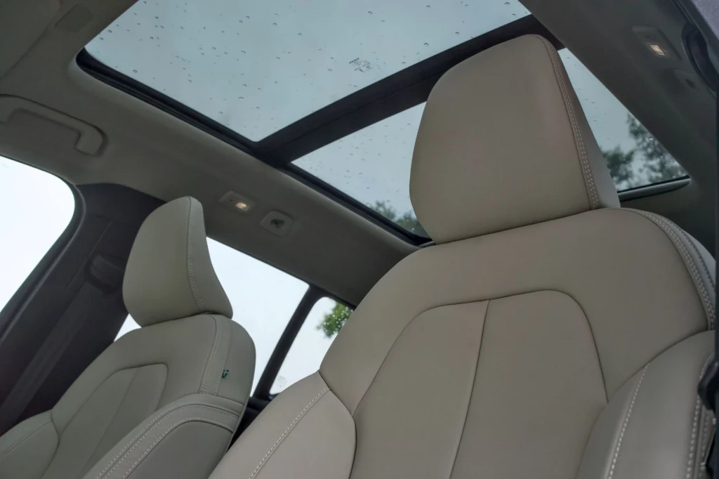 Volvo XC40 może być także wyposażone w panoramiczny dach. Jasne, skórzane fotele samochodowe z widocznym panoramicznym dachem szklanym oraz fragmentami wnętrza nowoczesnego pojazdu.