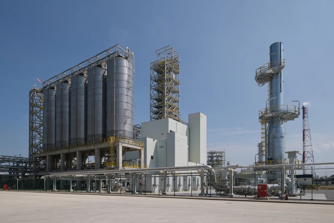 Fabryka Grupy Azoty Projekt Polimery Police (zdjęcie z 2023 roku) Kompleks przemysłowy z kilkoma dużymi cylindrycznymi zbiornikami, rurami oraz wieżą technologiczną na otwartym terenie pod błękitnym niebem.