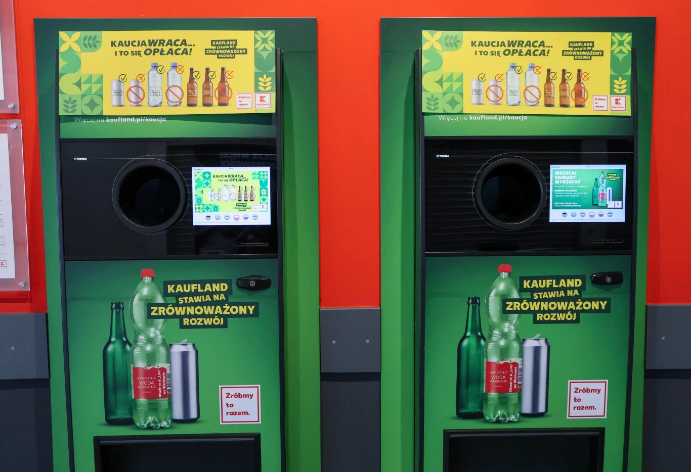 Dwie zielone maszyny do zwrotu butelek i puszek ustawione obok siebie, każda z ekranem dotykowym i otworem na opakowania, napisy promujące recykling oraz zrównoważony rozwój, logo sieci Kaufland.