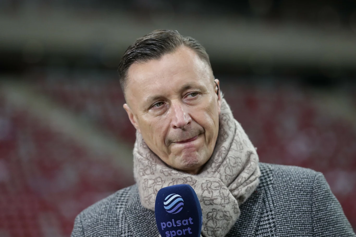 Tomasz Hajto Mężczyzna w szarym płaszczu i szaliku udziela wywiadu na stadionie, trzymając mikrofon Polsat Sport.