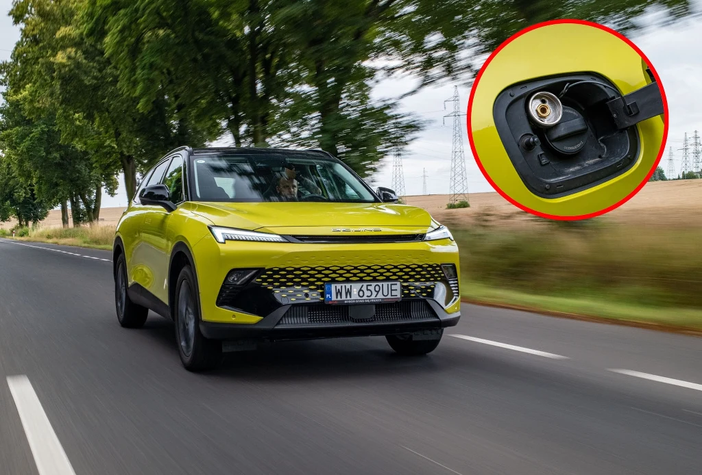 Jasnożółty nowoczesny SUV jedzie drogą pośród pól, na bocznym pasie, zbliżenie na port ładowania elektrycznego wyróżnione w czerwonym okręgu.