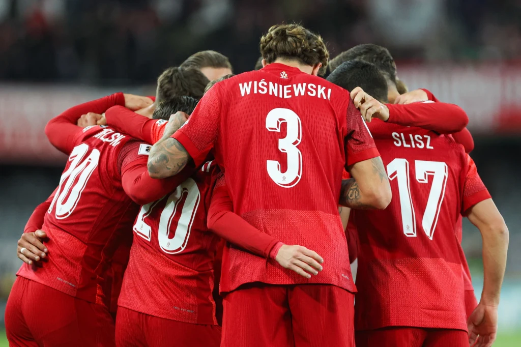 reprezentacja Polski Grupa piłkarzy w czerwonych strojach przytula się w okręgu podczas meczu, tworząc zwartą drużynę, widoczne są nazwiska zawodników na plecach.