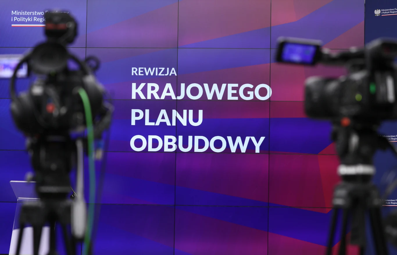 MRPiPS zatrudni eksperta i oferuje jedną z najwyższych pensji w administracji (zdj. ilustracyjne) Kamery ustawione przed wielkoformatowym ekranem z napisem 'Rewizja Krajowego Planu Odbudowy' na tle w kolorach niebiesko-czerwonych, po lewej stronie widoczne logo ministerstwa.