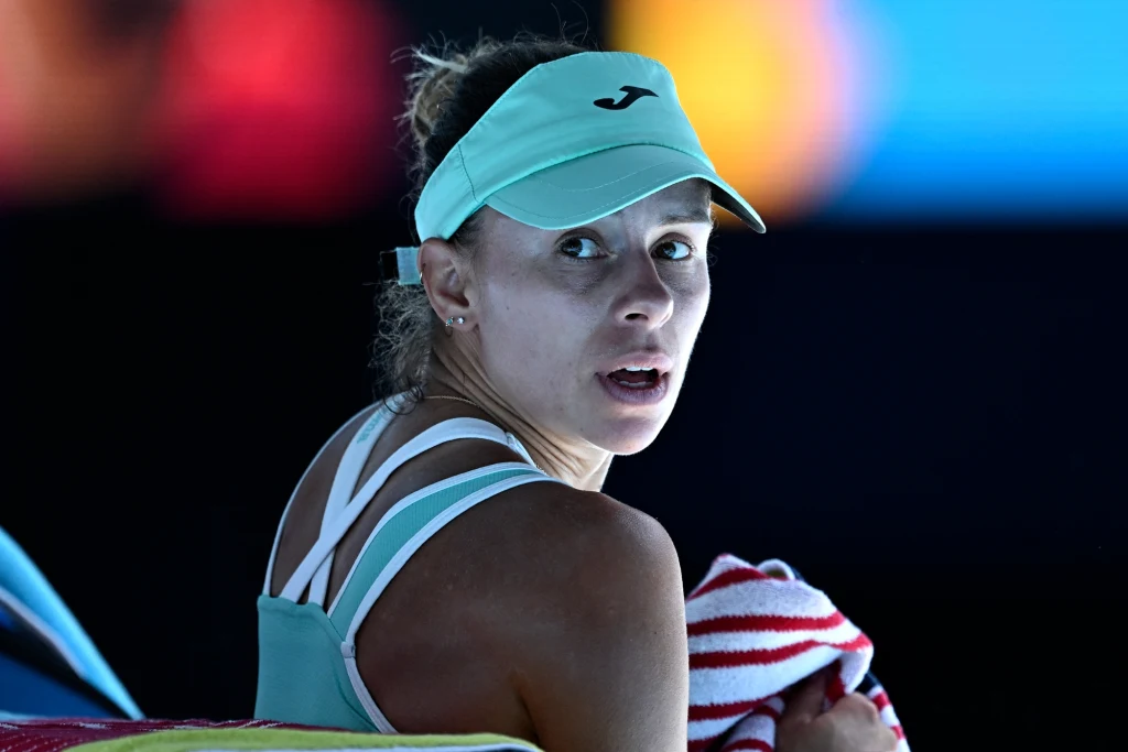 Magda Linette Tenisistka w czapce z daszkiem i sportowym stroju siedzi z ręcznikiem w dłoniach, spoglądając w stronę obiektywu, w tle rozmyte kolorowe światła.