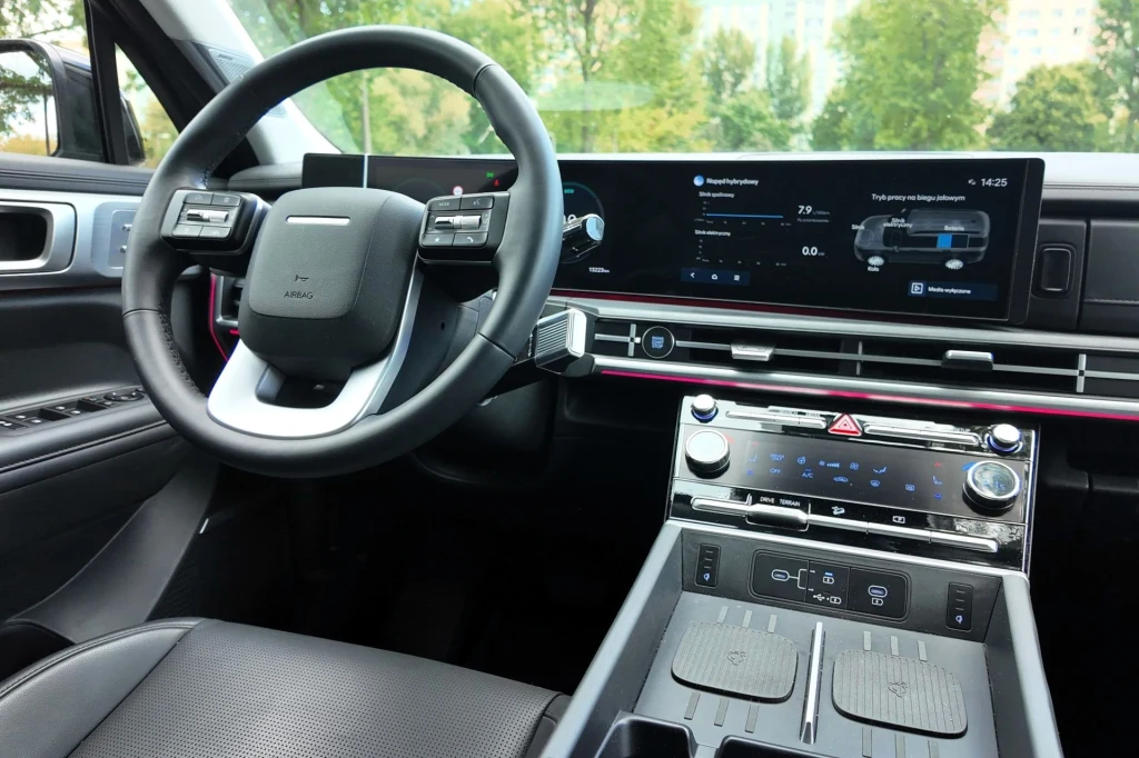 Nowoczesna deska rozdzielcza samochodu z dużymi ekranami cyfrowymi, kierownicą o ciekawym designie oraz panelem sterowania rozmieszczonym centralnie.