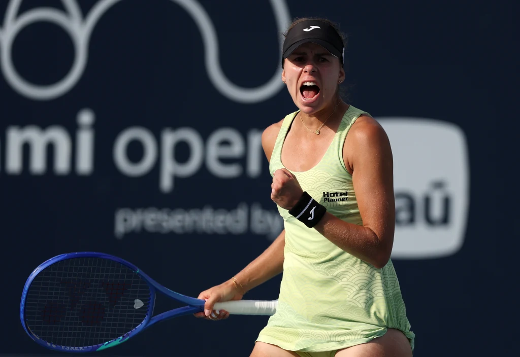 Magda Linette Tenisistka w żółtym stroju sportowym celebrująca punkt na korcie, z widocznym wyrazem radości i determinacji na twarzy, w tle logo zawodów Miami Open.
