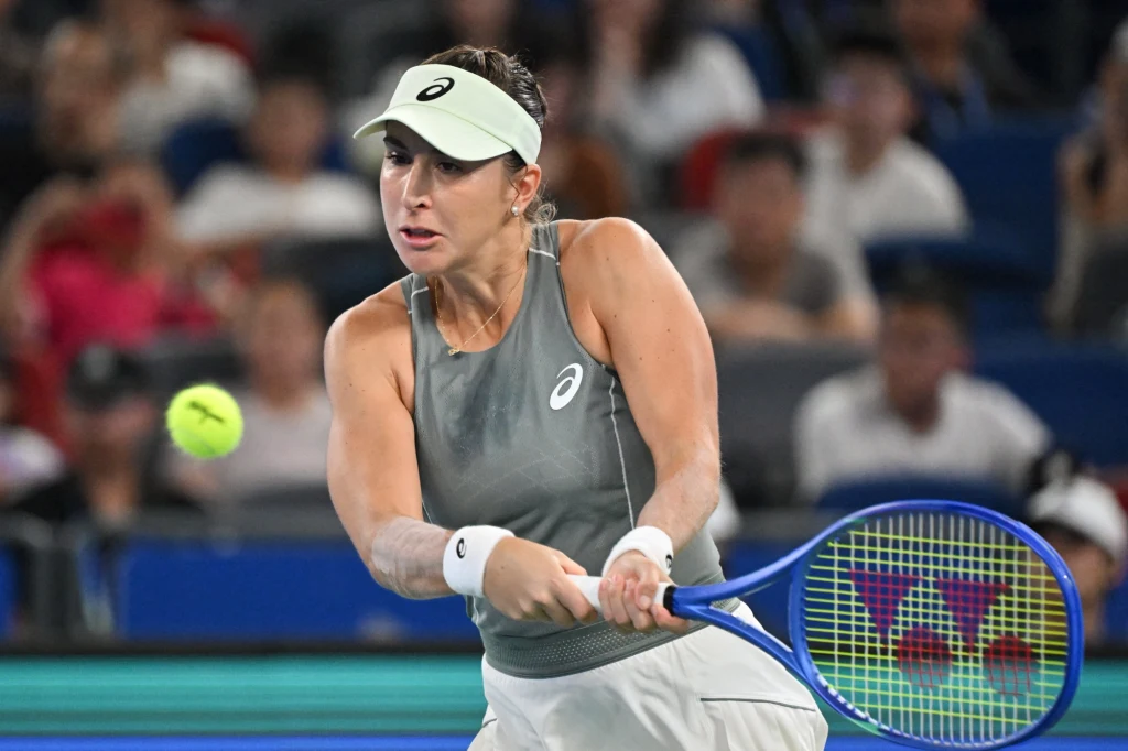Belinda Bencic Tenisistka w sportowym stroju skoncentrowana na wykonaniu backhandowego uderzenia podczas meczu, wokół widownia na trybunach i dynamicznie lecąca piłka tenisowa.