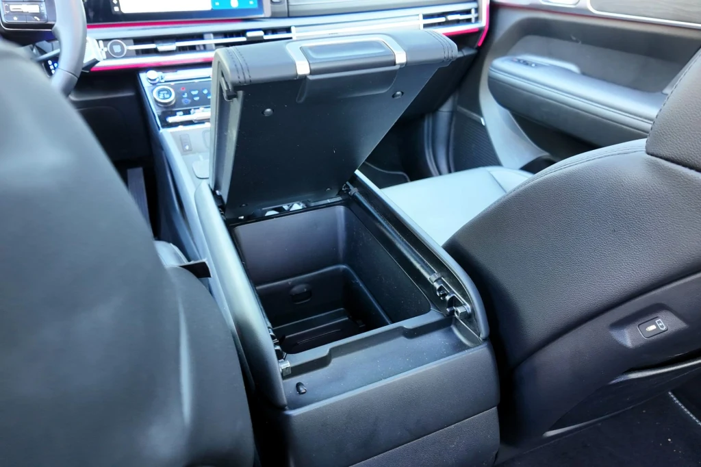 Wnętrze samochodu z otwartym schowkiem w podłokietniku środkowym pomiędzy przednimi fotelami, widoczna deska rozdzielcza z panelem sterowania oraz elementy siedzeń.