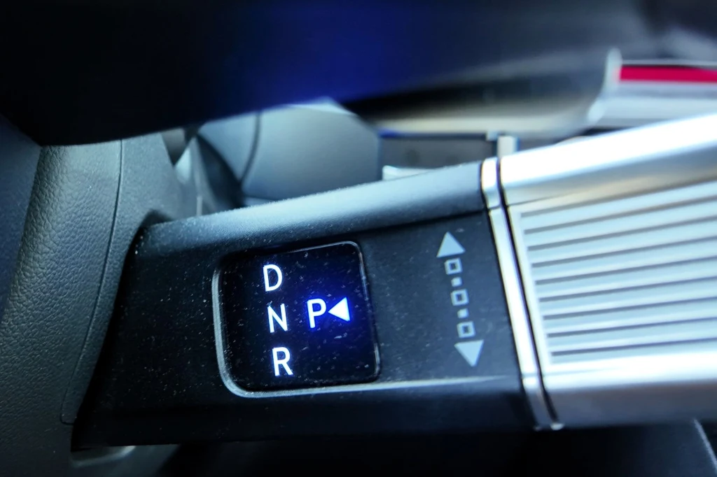 Elektroniczny selektor biegów w samochodzie z wyraźnie podświetlonymi symbolami D, N, R i P oraz strzałkami wskazującymi kierunek zmiany trybu.