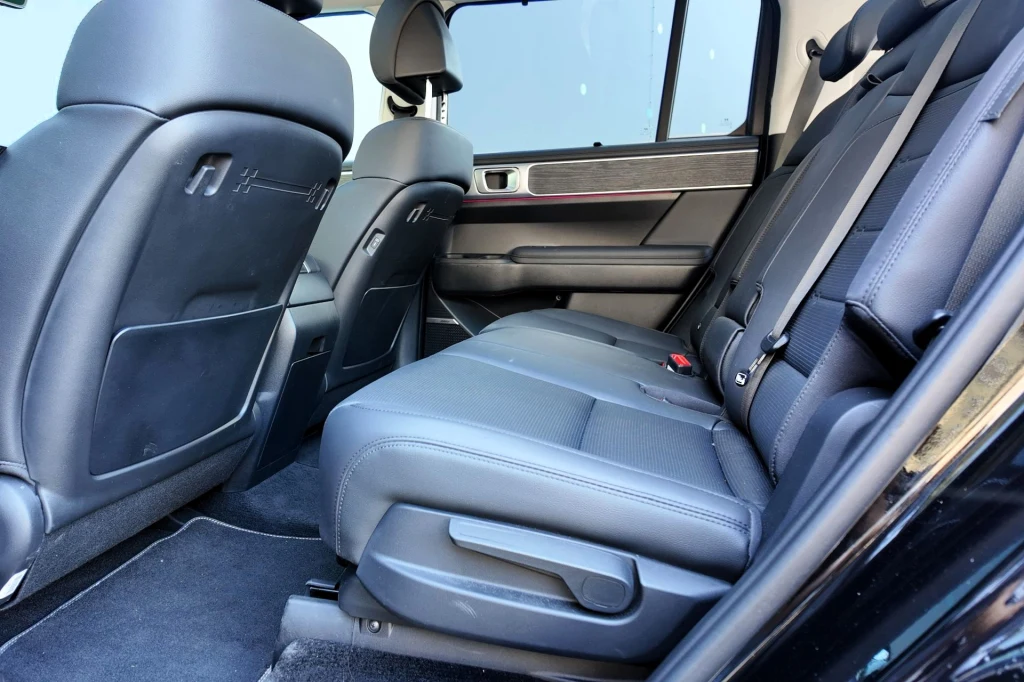 Tylny rząd czarnych, skórzanych siedzeń w samochodzie osobowym, szerokie siedzisko, podłokietnik, eleganckie wykończenie wnętrza i widoczne pasy bezpieczeństwa.