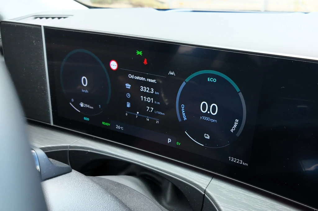 Cyfrowy wyświetlacz deski rozdzielczej samochodu prezentujący informacje dotyczące przebiegu, prędkości, poziomu energii, zużycia paliwa oraz trybu jazdy ECO, z podziałem na czytelne wskaźniki oraz cyfrowe grafiki.