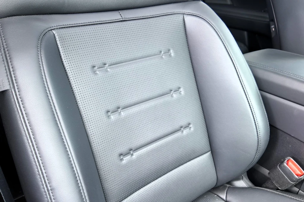 Grafitowa, skórzana tapicerka samochodowego fotela z poziomymi przeszyciami i perforacjami, widoczny fragment oparcia i siedziska oraz pas bezpieczeństwa po prawej stronie.