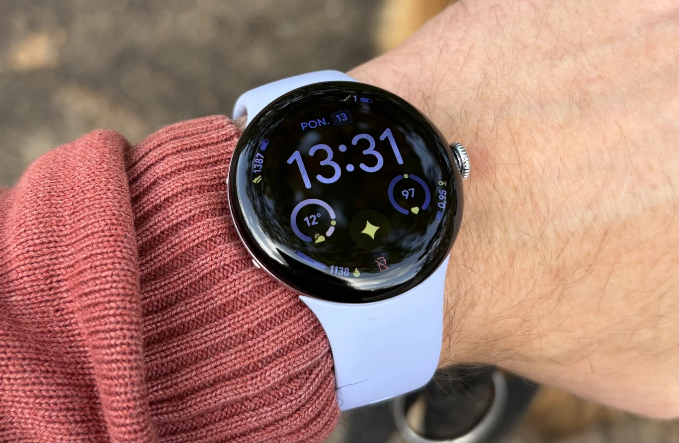 Test Google Pixel Watch 4. Ewolucja w dobrym kierunku. Smartwatch z okrągłym wyświetlaczem na nadgarstku osoby ubrane w różową bluzę, ekran pokazuje godzinę 13:31 w poniedziałek wraz z dodatkowymi wskaźnikami aktywności i pogody.