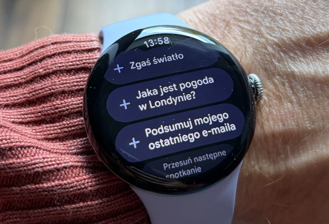 Google Pixel Watch 4 daje prosty dostęp do Gemini i użytkownicy mogą tworzyć własne skróty dla AI. Inteligentny zegarek na nadgarstku prezentujący ekran z listą poleceń głosowych, na wyświetlaczu widoczne pytania dotyczące pogody, zarządzania światłem, podsumowania e-maili oraz spotkań.